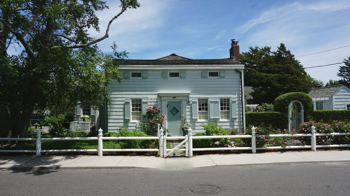 A shingled cottage with a white picket fence and climbing roses in Greenport, Long Island