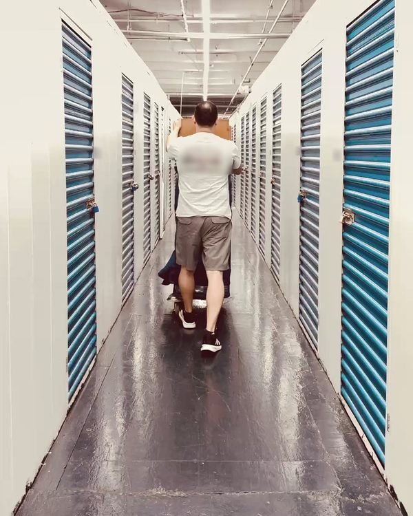 A mover wheeling a load down a storage-unit corridor with blue roll-up doors